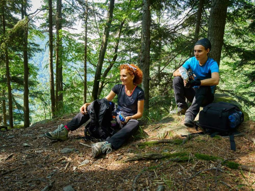 Two walkers taking a rest break in the shade on a wooded trail.
